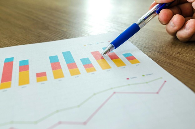 Hand pointing at printed bar and line charts with a pen on a wooden table.